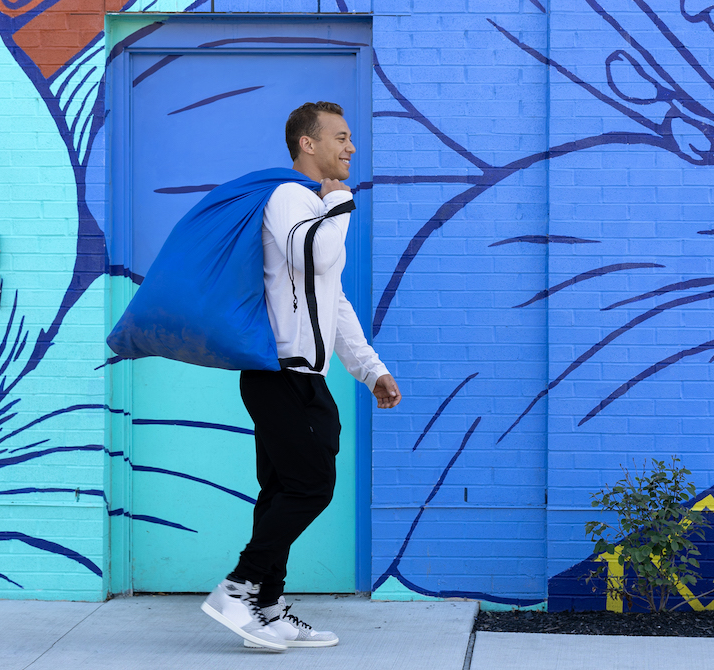 Man with blue Push Laundry bag walking in front of a colorful mural