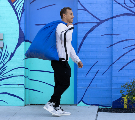 Man with blue Push Laundry bag walking in front of a colorful mural